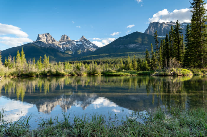 Still water reflecting the Three Sisters peaks near Canmore in soft evening light