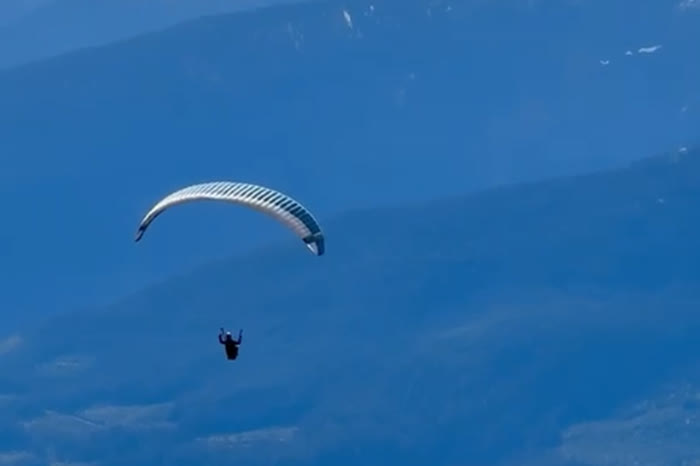 A paraglider flying in open sky above mountains and cloud