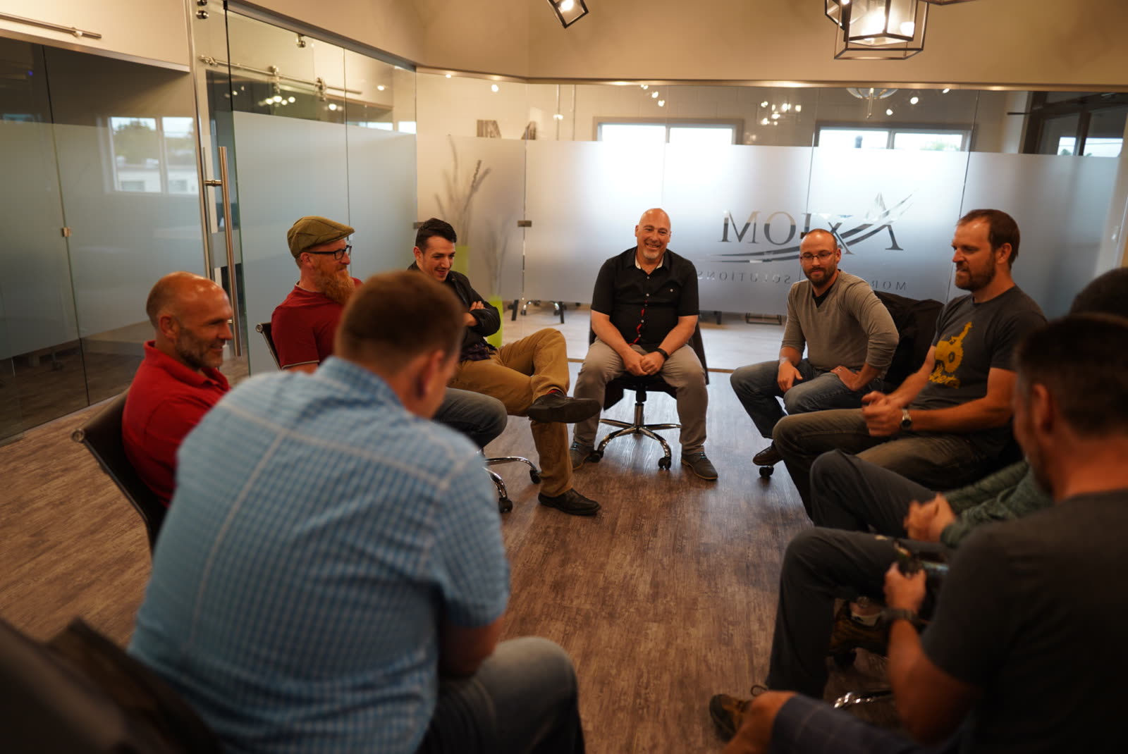 Men sitting together in a circle of chairs at a Connect'd Men gathering, talking and smiling